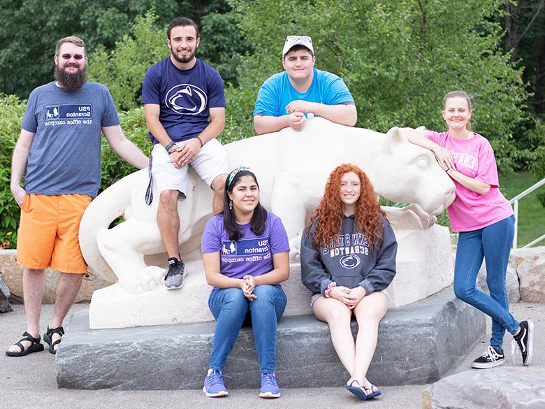 six students gather around lion shrine statue